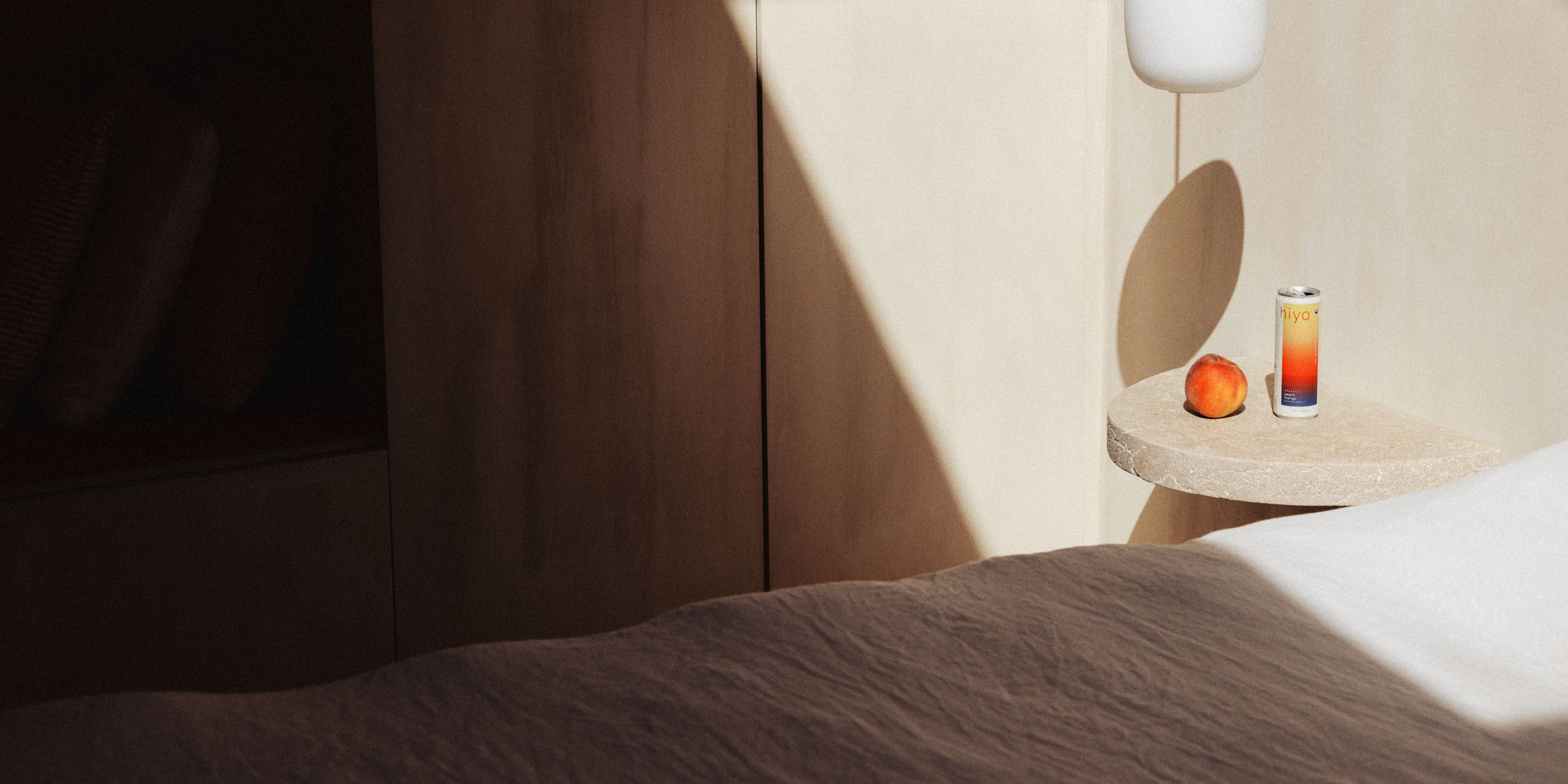 a peach mango hiyo can sitting atop a bedside table with a fresh peach next to it.